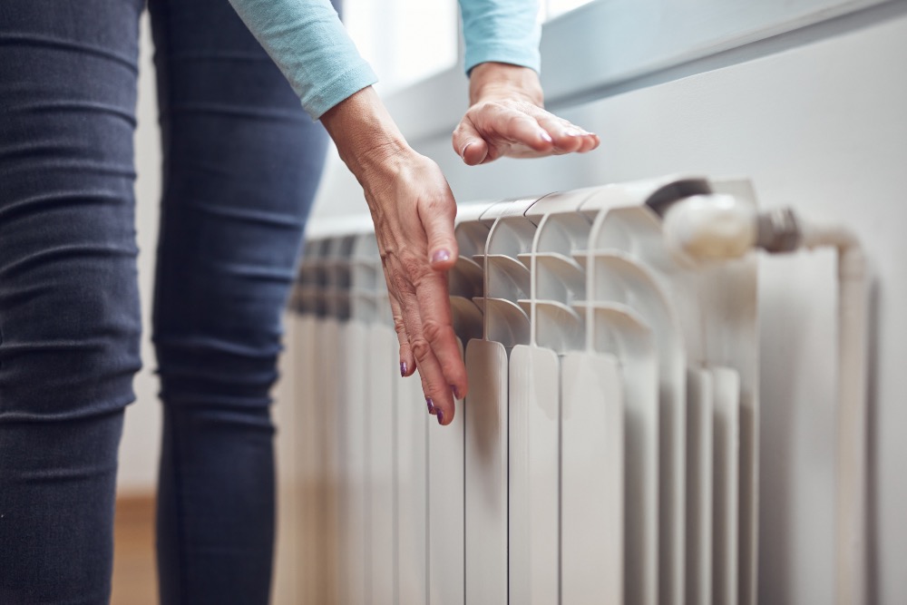 Person feeling their radiator for heat with a white radiator on a white wall