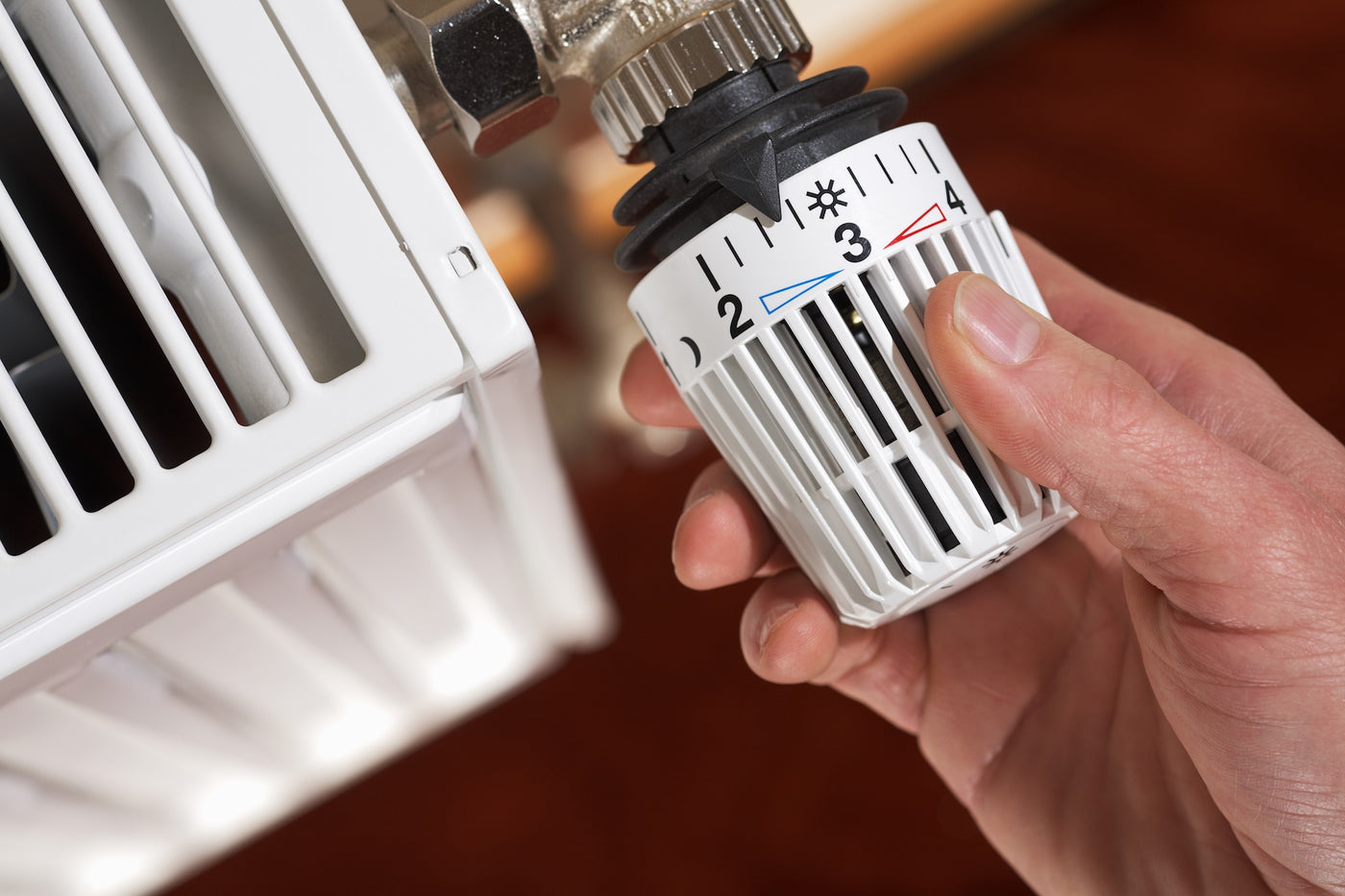 Hand turning a thermostatic radiator valve on a white radiator, with settings marked from frost protection to four.