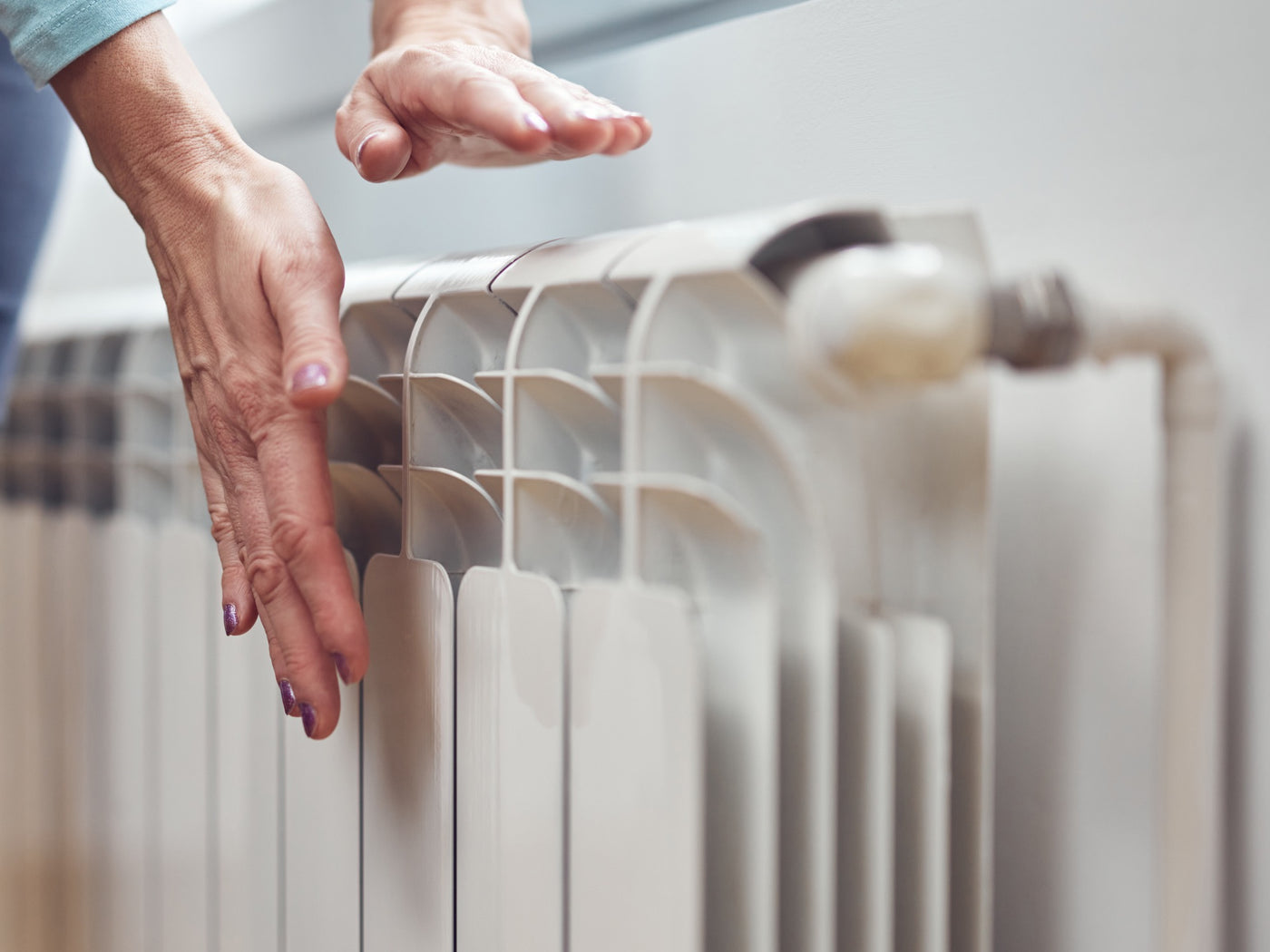Person holding their hands near a white radiator to check whether it is warm.