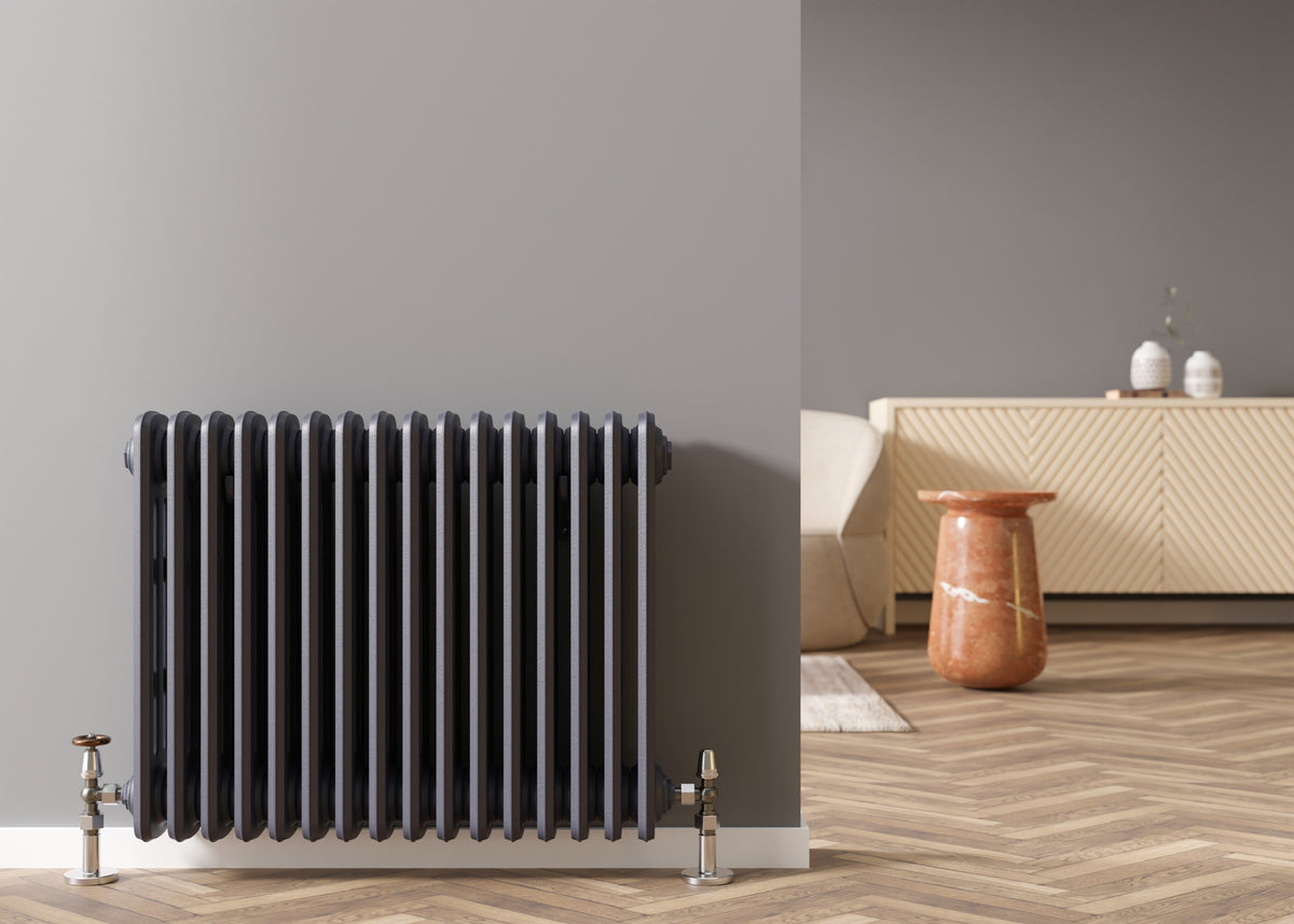 Black column radiator with chrome valves in a contemporary living room with herringbone wood flooring.