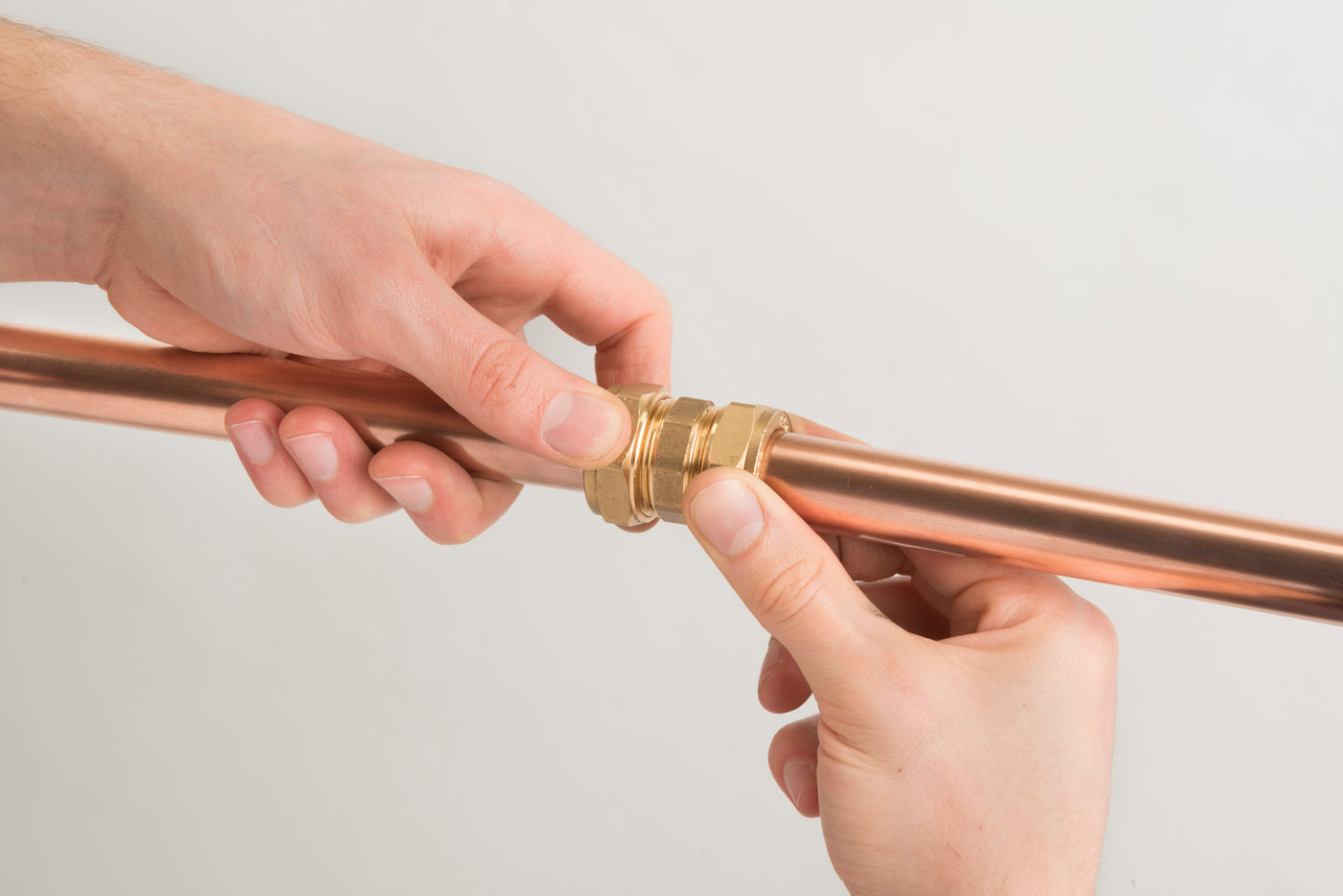 Hands supporting an assembled brass compression coupling on a copper pipe.
