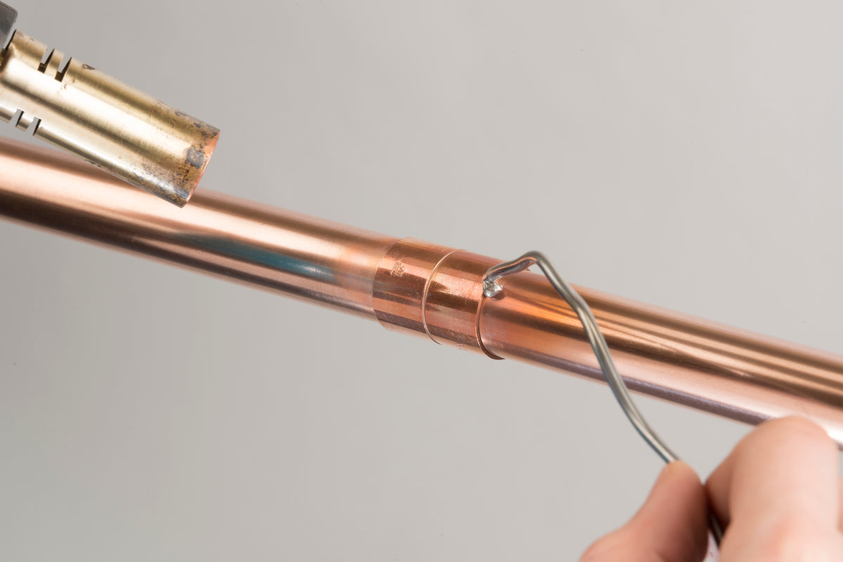 Solder wire applied to an end-feed fitting joining two copper pipes, ready for heating with a blowtorch.