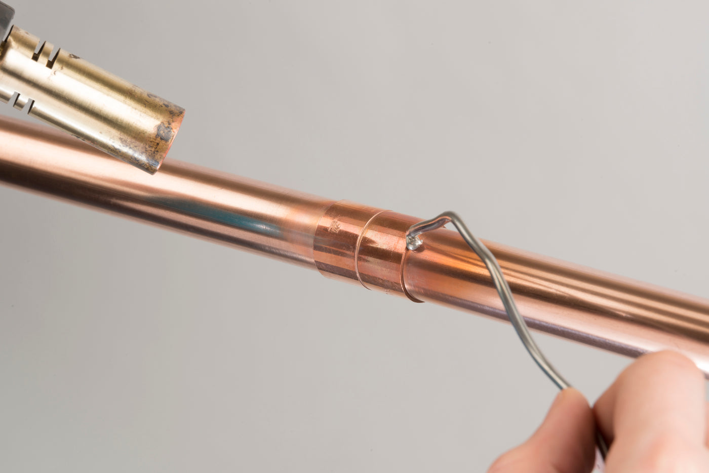 Solder wire applied to an end-feed fitting joining two copper pipes, ready for heating with a blowtorch.