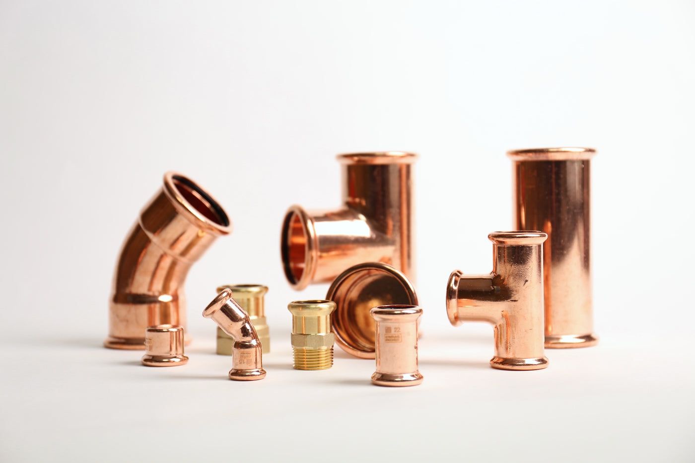Assorted copper press fittings, including elbows, tees, couplings and threaded adaptors, on a white background.