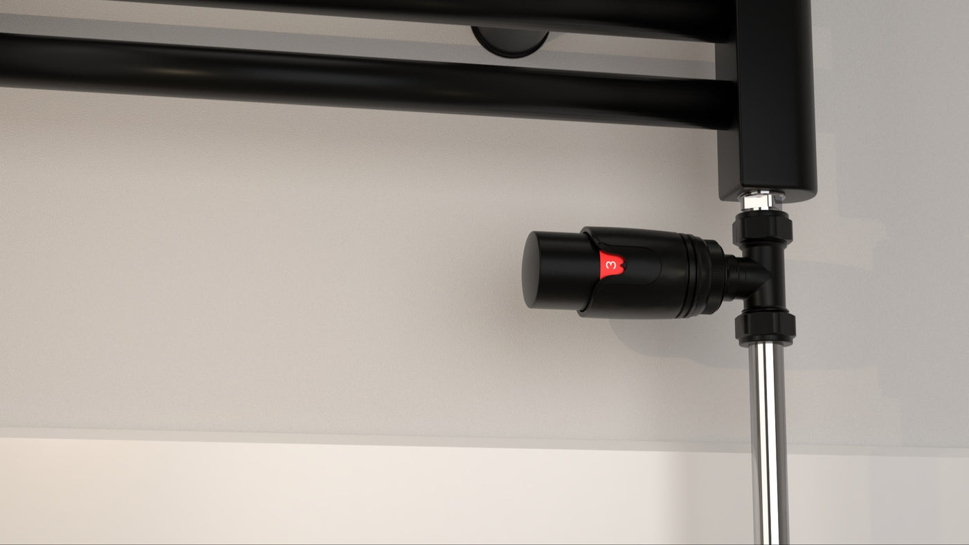 Black straight thermostatic valve, set to level three, connecting floor pipes to the bottom of a black radiator.