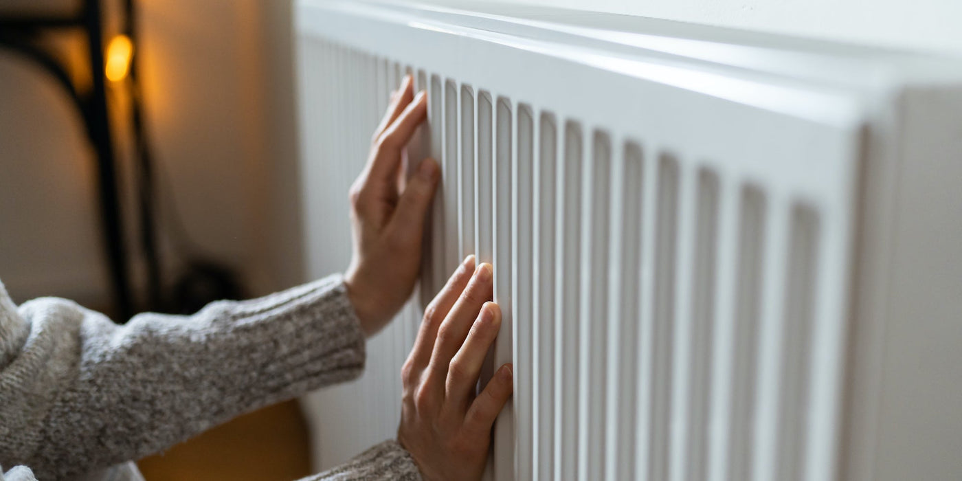 Hands feeling the surface of a white panel radiator to check whether it is heating evenly across the front.