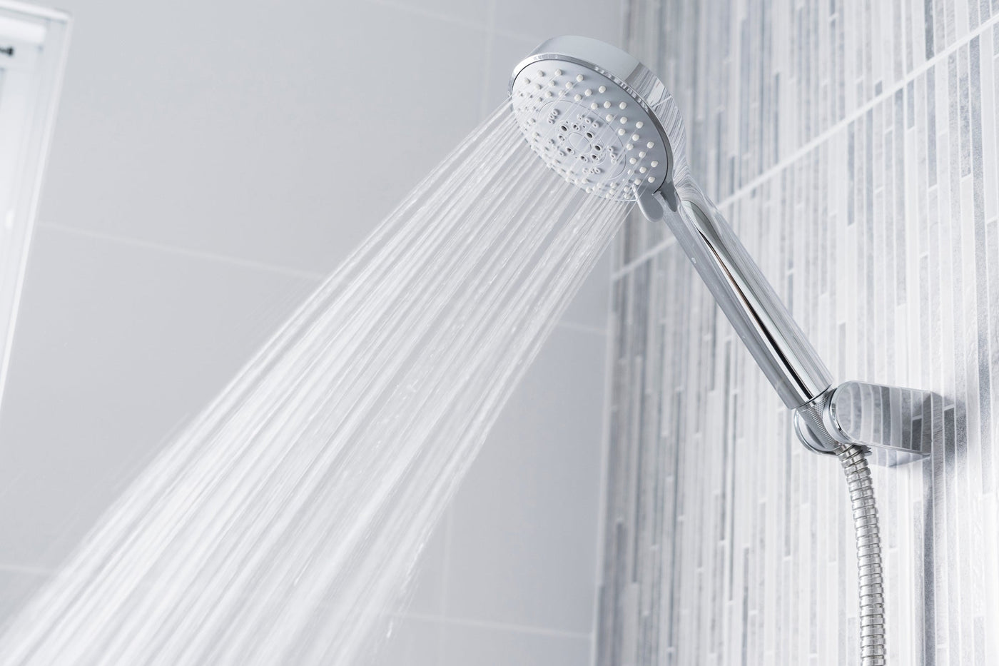 Chrome handheld shower head producing a strong, even spray of water in a modern tiled shower enclosure.