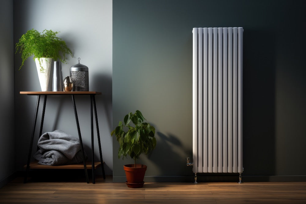 White vertical column radiator installed against a dark feature wall in a contemporary room with wooden flooring, houseplants and a side table.