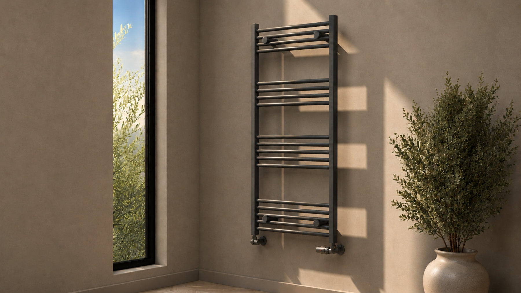 Wide view of an anthracite heated towel rail with matching corner valves in a sunlit bathroom beside a tall window and potted plant.